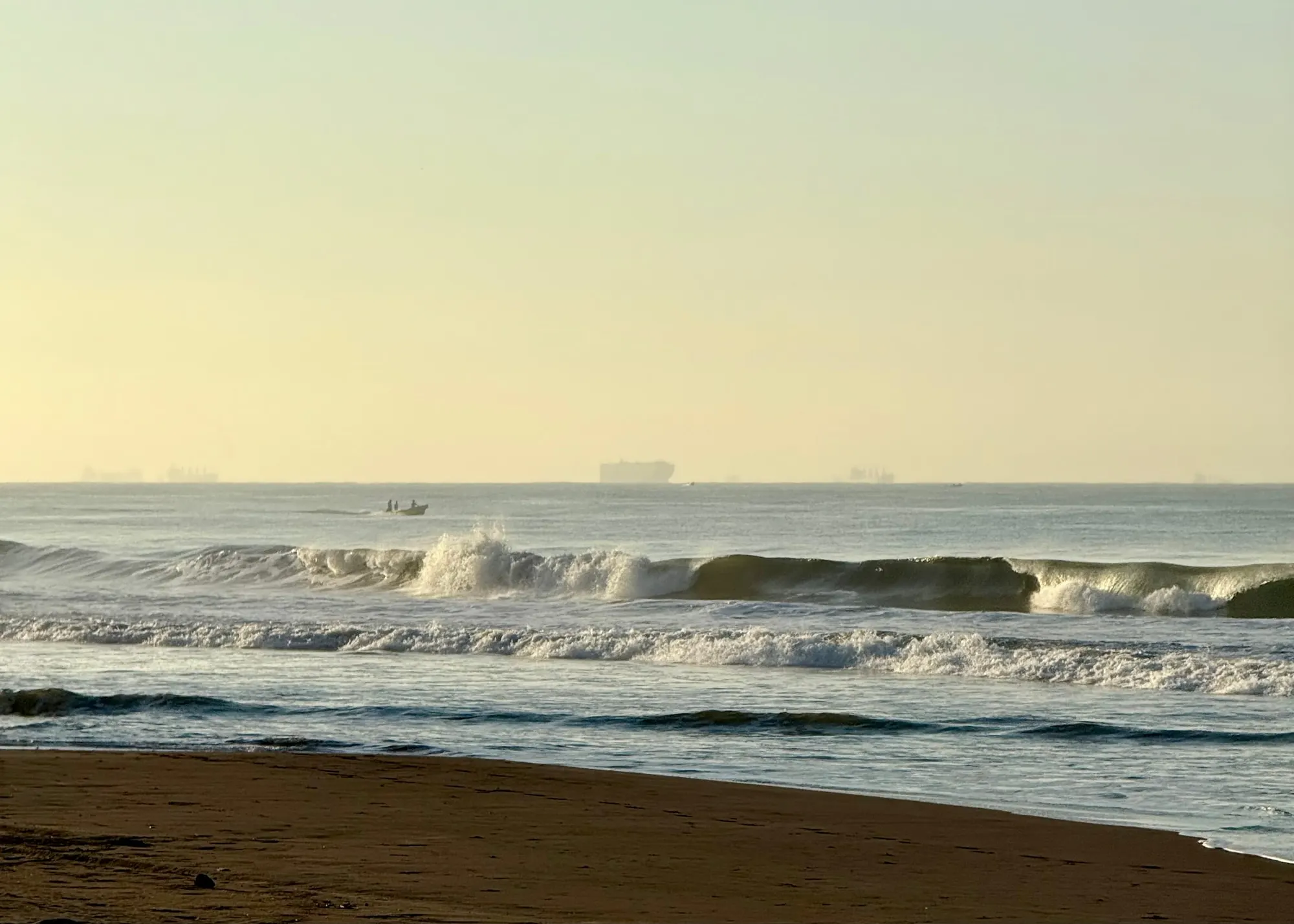 Two people walking a wide Pacific beach at sunset near Barra de Santiago