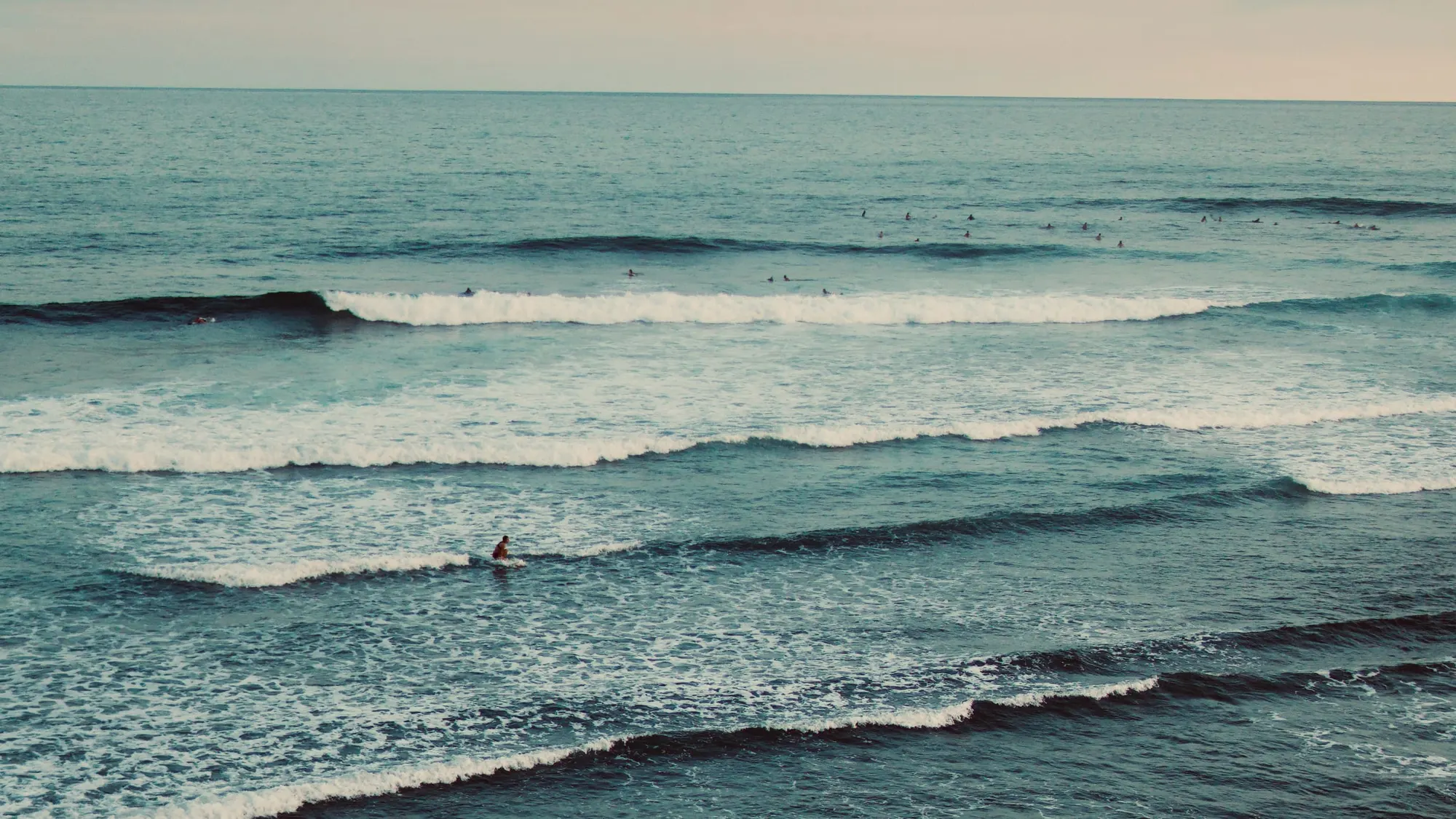 Several lines of swell peeling toward shore at El Sunzal, with a crowd of surfers sitting out the back and one rider up on an inside wave