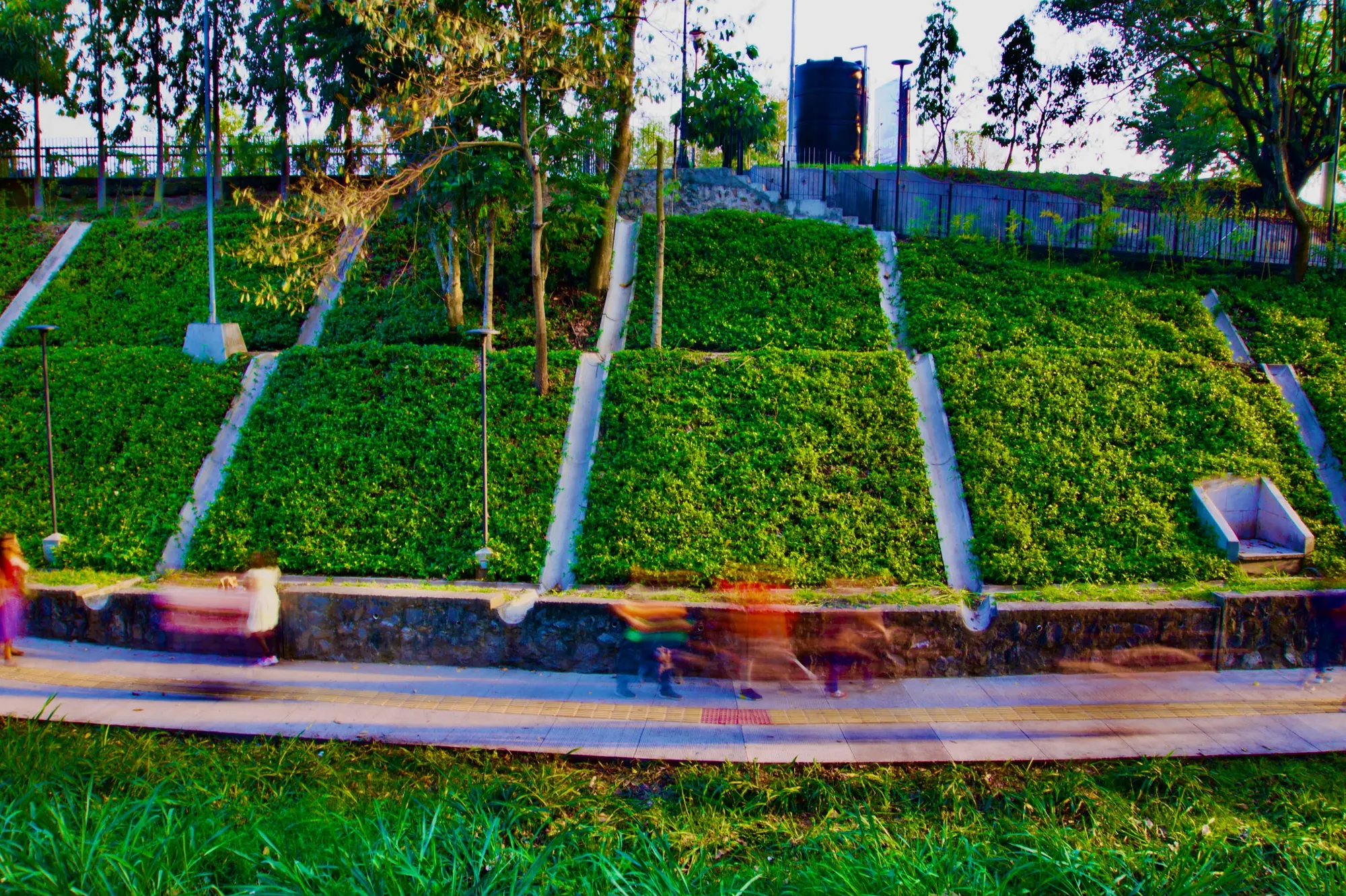 Terraced grass steps at Parque Bicentenario, cut by concrete channels, with people walking along the path below